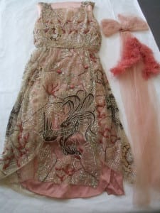 1920s pink beaded net evening dress laid flat with sash and feather trim accessories, after conservation treatment.