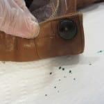 Gloved hand holding leather jacket cuff showing corroded metal button with green residue.