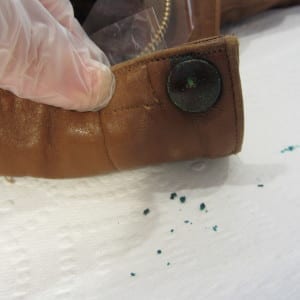 Gloved hand holding leather jacket cuff showing corroded metal button with green residue.