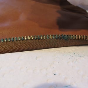 Heavily corroded brass zipper teeth on a leather flight suit.