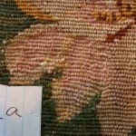 Conservation documentation photo labeled "2a" showing the same floral needlework area after treatment, with the previously damaged hole now stabilized and re-woven with blended pink and tan wool stitching matching the surrounding pattern.