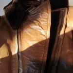 The collar and front closure area of a tan leather flight suit after conservation, showing the dark brown fur-lined collar, cleaned brass zipper.