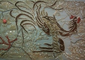 Post-conservation detail of the dragon motif on a pale blue net evening dress, showing the brown velvet and gold metallic thread appliqué re-stabilized and outlined with seed beads.