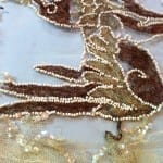 A dragon tail motif on a sheer net evening dress showing brown velvet appliqué outlined with seed bead strands, after conservation treatment.