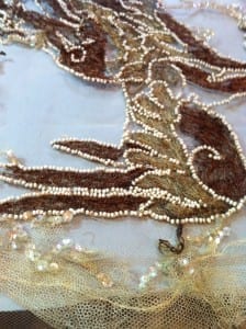 A dragon tail motif on a sheer net evening dress showing brown velvet appliqué outlined with seed bead strands, after conservation treatment.